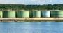 Large industrial green fuel storage tanks by the edge of a body of water